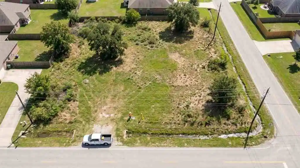 An aerial drone view of a surveyor inspecting a vacant suburban land parcel beside a road - sell my land fast in Houston - 2